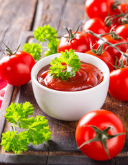 Bowl of tomato sauce and cherry tomatoes on wooden table.