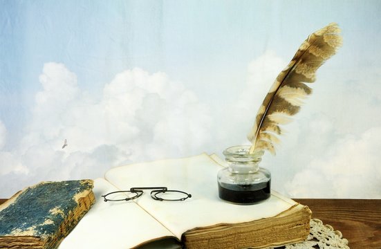 Desk with old books, pince-nez and inkwell on background of sky