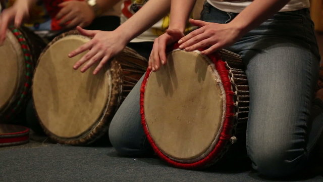 Girls playing on ethnic drums djembe, holding drums between legs
