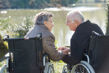 Elderly couple in wheelchairs, reaching for eachother