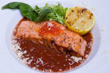 Salmon in red tomato sauce with caviar in white plate