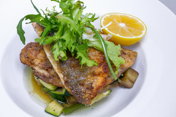 Cooked dorado fish with vegetables and lemon in white plate