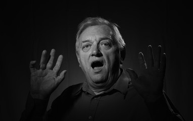 Black and white portrait image of a mature man with a shocked facial expression and his hands in the air. 