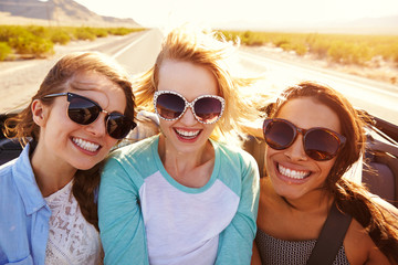 Three Female Friends On Road Trip In Back Of Convertible Car