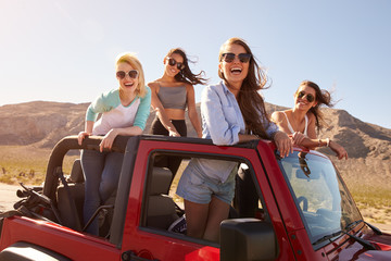 Four Female Friends On Road Trip Standing In Convertible Car