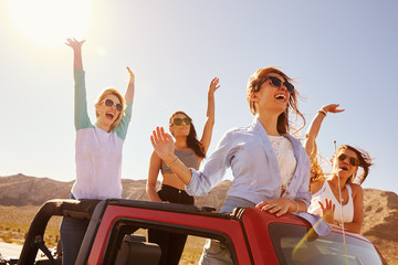 Four Female Friends On Road Trip Standing In Convertible Car