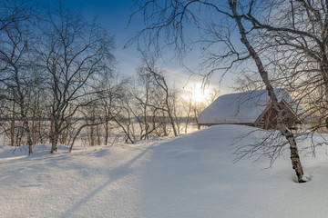 Snow Covered House and bare trees on field during sunrise
