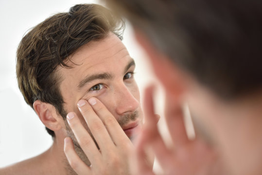Handsome man applying facial cream in front of mirror