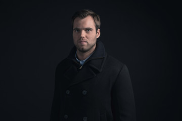 Stubbly bearded young man wearing dark blue winter coat.