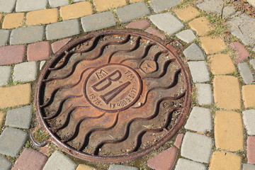 Rusted manhole on a street with pavement from multicolor block