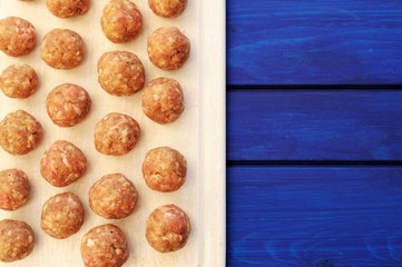Raw homemade meatballs on white plastic cutting board with copys
