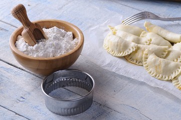 Raw dumplings, bowl with flour and cutter on wooden table