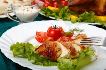 Sliced roasted chicken breast and served with fresh vegetables on white plate close up