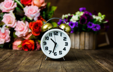 White alarm clock on wooden table with  vintage flower backgroun