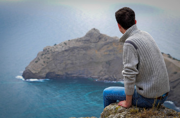 Young man sitting looking at the sea and the mountains