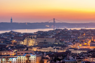 Sunset with orange tones from the Monte Agudo viewpoint in Lisbon, capital of Portugal. In the background the 25th of April Bridge and The Christ the King statue, symbols of the city
