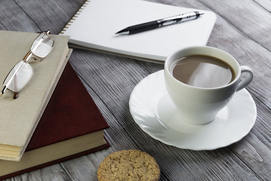 two books, white porcelain cup of coffee with milk and a saucer