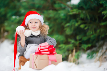 Happy little girl in santa hat with christmas box gift in winter day outdoors on Xmas eve