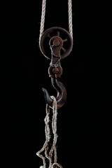 Big metal hook hanging on rope isolated on black background.