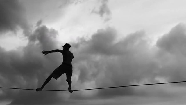 Silhouette of person on slackline in slow motion against cloudy skies in black and white