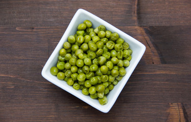 Cooked peas on square bowl on wooden table seen from above