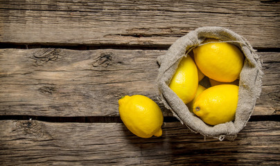 Fresh lemons into an old bag. On wooden background.