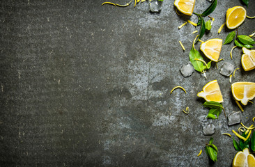 Slices of lemon, ice, leaves on stone table.