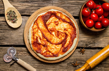 The rolled out pizza dough with tomato sauce, rolling pin and spices.
