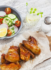 Spicy chicken wings and fresh vegetable salad on wooden white background