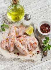 Raw ingredients to prepare spicy chicken wings, spices, salt, parsley, chicken wings on a light wooden table