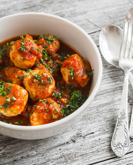 chicken meatballs with tomato sauce in a white bowl on bright wooden surface. Healthy food