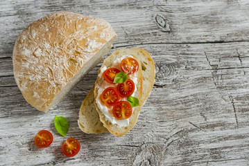 Freshly baked rustic bread and  sandwich with ricotta, tomato and basil on a light wooden board