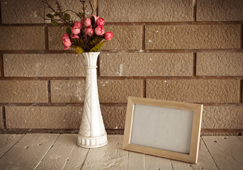 Photo frame and flowers on wooden table over wall background 