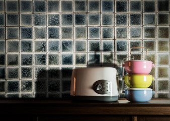 Colorful tiffin carrier and toaster on wooden cupboard