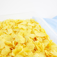 The close up of tasty golden corn flakes in plastic container box on blue cotton fabric.