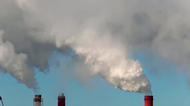 Sunlit puffy clouds of pure steam from three stacks on light blue sky background. Dioxide carbon and warm, exhausting with the industry chimneys in the atmosphere, is the great danger for ecology.
