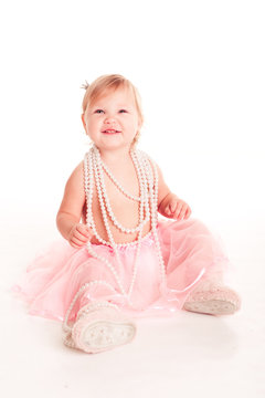 Laughing baby girl 1-2 year old sitting on floor over white. Wearing skirt and pearl necklace. Childhood.