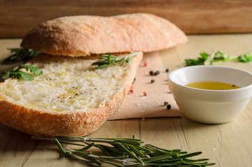 Sliced bread ciabatta watered with extra virgin olive oil with herbs  on wooden background