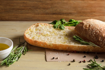 Sliced bread ciabatta watered with extra virgin olive oil with herbs  on wooden background