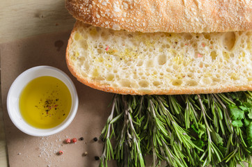 Sliced bread ciabatta watered with extra virgin olive oil with herbs  on wooden background. View...