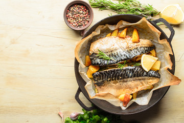 Baked fish mackerel with baked potato in a pan, rosemary, lemon and spice on a wooden background