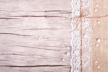 Lace, pearls, bowknot, canvas, sackcloth on wooden background. Rustic design. Free space for your...