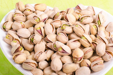 Salt pistachios on the white plate on green background.