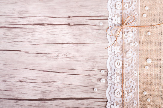 Lace, pearls, bowknot, canvas, sackcloth on wooden background. Rustic design. Free space for your text