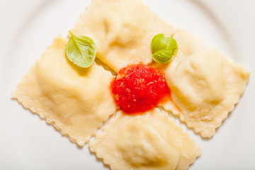 Russian ravioli - pelmeni with tomato sauce and basil on a white