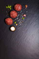 Raw ground beef meat steak cutlets with herbs and spices on blac