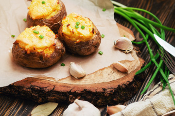 
hearty and healthy dinner , baked potatoes in their skins with cheese , herbs , spices and garlic on a wooden background
