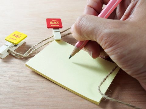 Taking note on yellow paper with attached red wooden paper clip, Saturday tag
