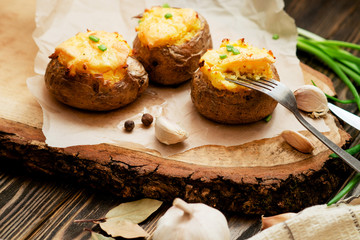 
hearty and healthy dinner , baked potatoes in their skins with cheese , herbs , spices and garlic on a wooden background