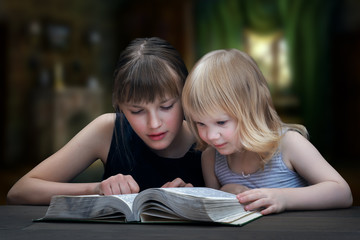 Дети читают книгу. Две девочки, две сестры вместе. В...